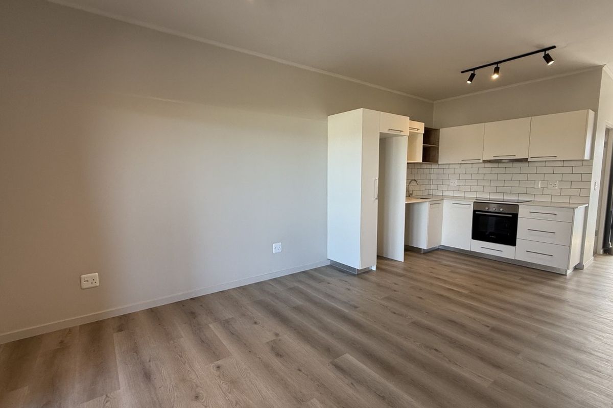 Modern open-plan kitchen and living area featuring sleek white cabinetry, subway tile backsplash, built-in oven, and durable laminate flooring with access to a balcony.