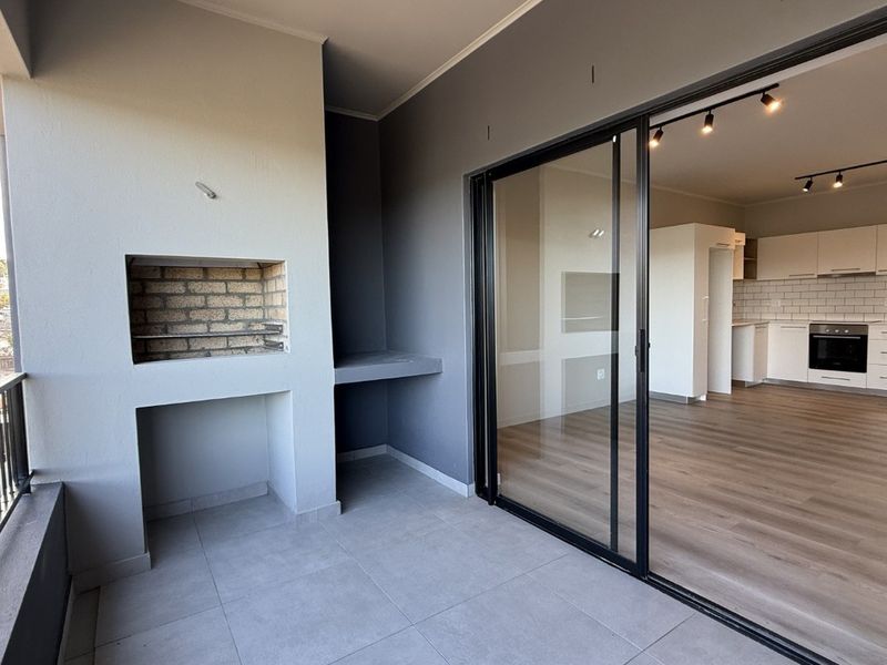 Covered balcony featuring a built-in braai, tiled flooring, and large sliding glass doors providing seamless access to the open-plan interior living area.