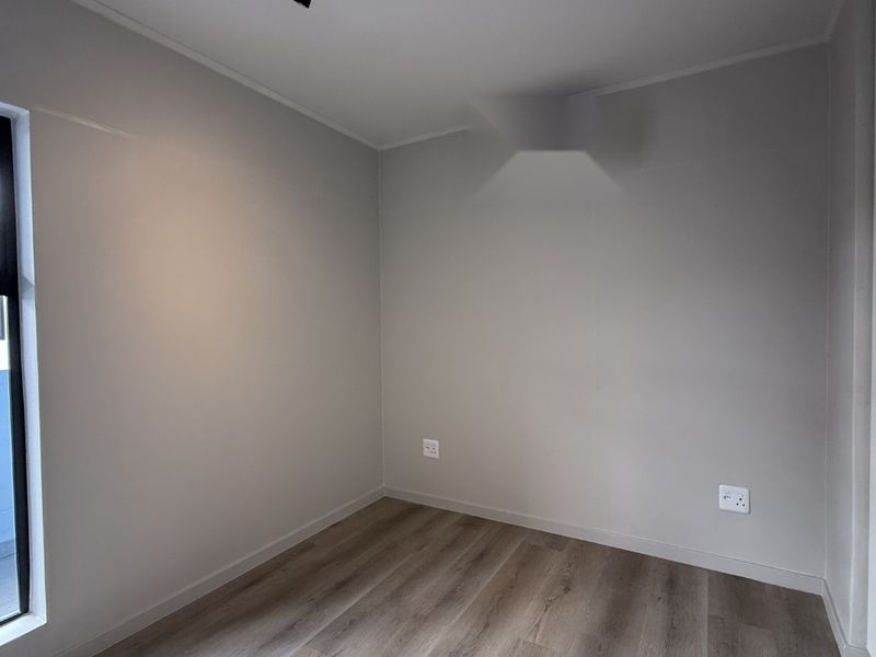 A clean, modern, and empty bedroom featuring neutral walls, laminate flooring, and a built-in cupboard, ready for personalization.