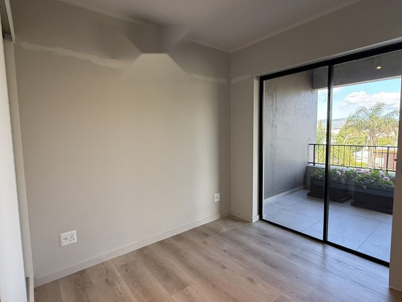 An empty bedroom featuring laminate flooring and a sliding glass door providing direct access to a private balcony.