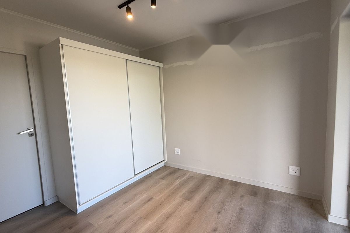 A bright, empty bedroom featuring modern laminate flooring, a built-in sliding door wardrobe, and track lighting, ready for personalization.