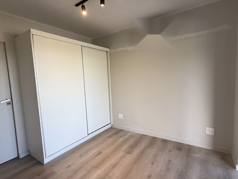 A bright, empty bedroom featuring modern laminate flooring, a built-in sliding door wardrobe, and track lighting, ready for personalization.