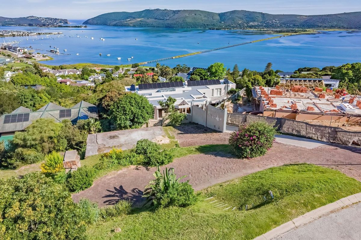 Aerial view of a vacant residential plot featuring a concrete driveway, retaining wall, and expansive views of the surrounding lagoon and landscape.