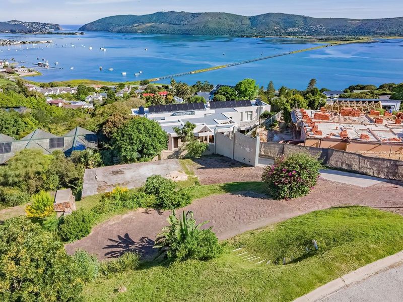 Aerial view of a vacant residential plot featuring a concrete driveway, retaining wall, and expansive views of the surrounding lagoon and landscape.