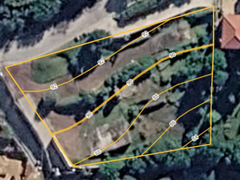 An aerial view of a vacant residential plot featuring overlaid topographic contour lines indicating the land's elevation profile.