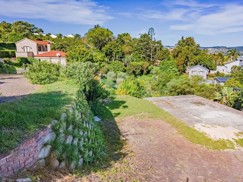 A sloped residential plot featuring a concrete slab foundation, established retaining walls, and mature garden surroundings in a quiet neighborhood setting.
