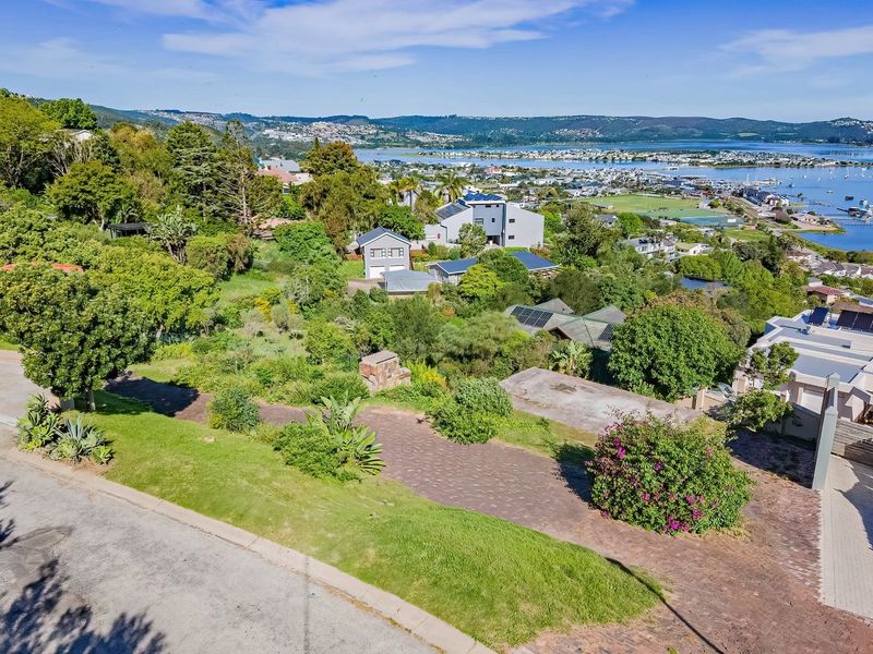 An elevated aerial view of a residential plot featuring a paved driveway, established garden, and scenic views of the surrounding coastal landscape.