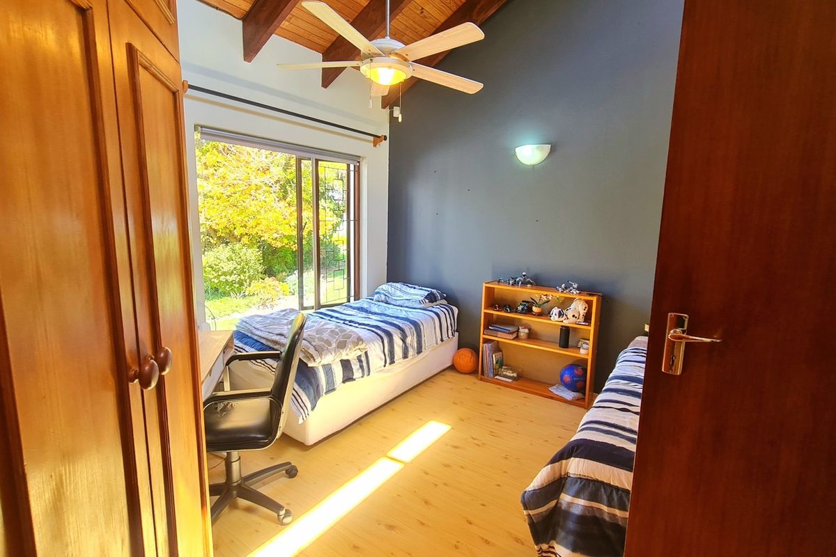 A bright bedroom featuring a vaulted timber ceiling with exposed beams, built-in wooden cupboards, laminate flooring, and a sliding glass door leading outdoors.