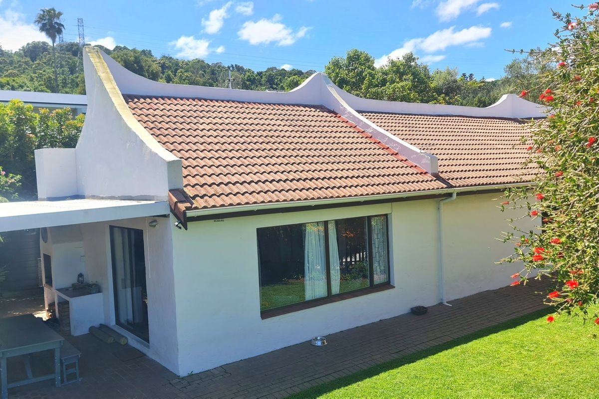 Rear view of the property featuring a classic gabled roof, paved patio area with a built-in braai, and well-maintained garden space.