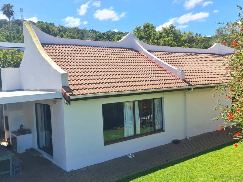 Rear view of the property featuring a classic gabled roof, paved patio area with a built-in braai, and well-maintained garden space.