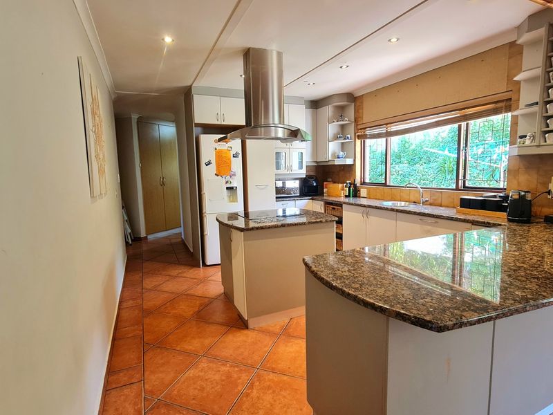 A functional kitchen featuring granite countertops, a central island with an extractor fan, ample cabinetry, and tiled flooring with a view of the garden.