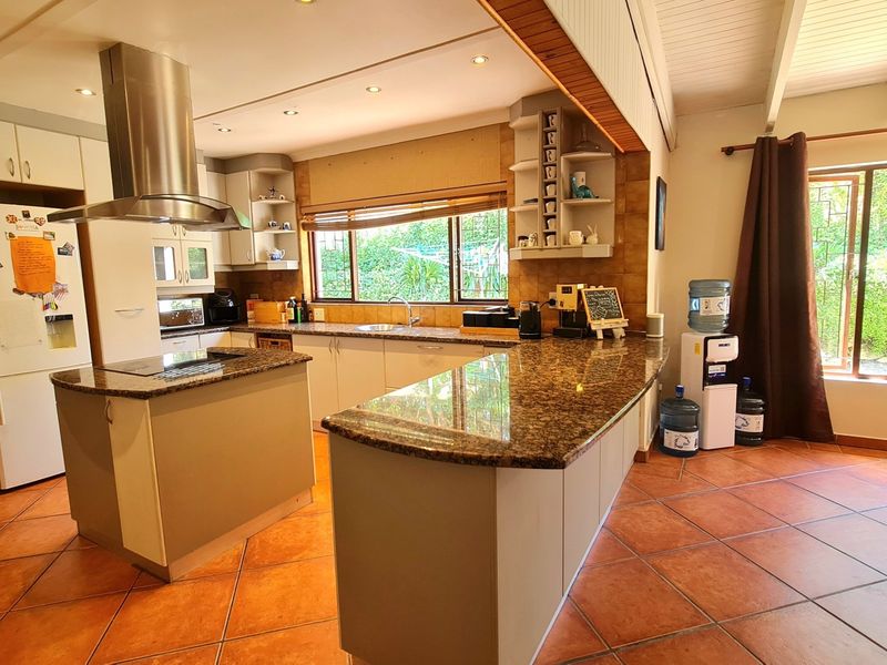 Spacious kitchen featuring granite countertops, a central island, stainless steel extractor fan, and tiled flooring with views of the garden.