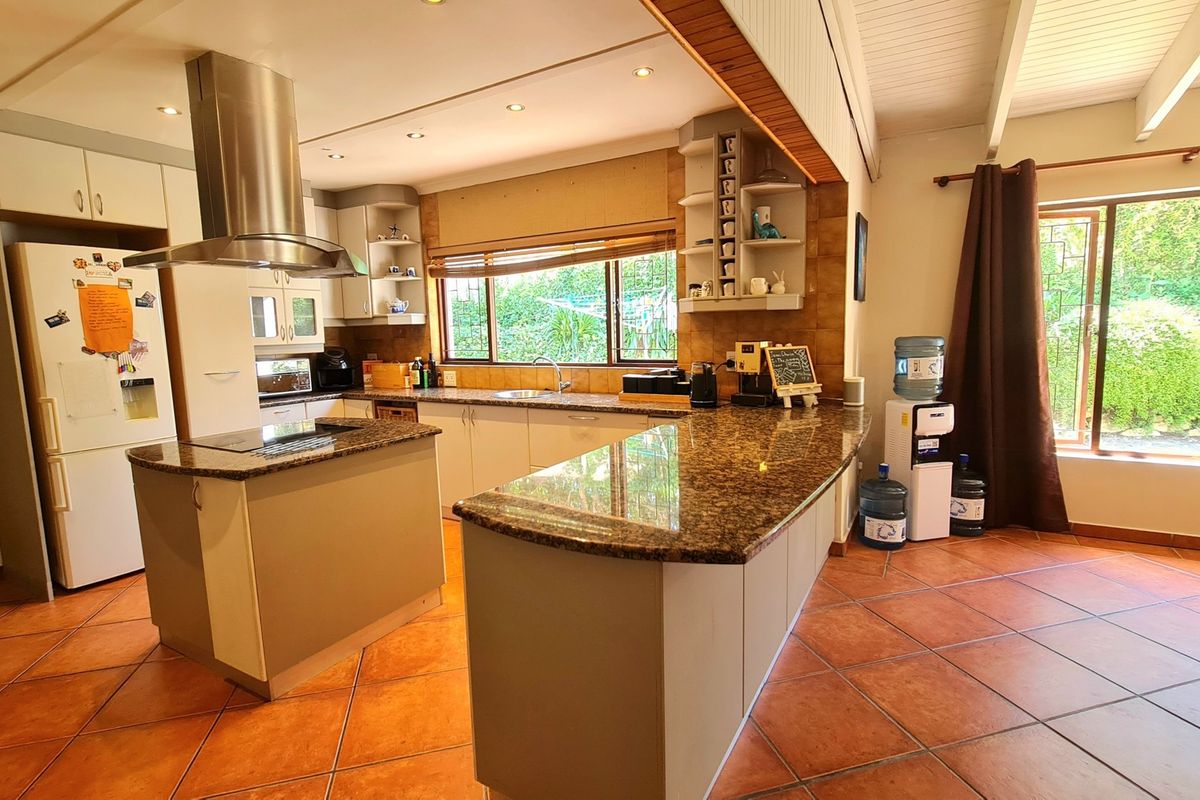 Spacious kitchen featuring granite countertops, a central island, stainless steel extractor fan, and tiled flooring with views of the garden.