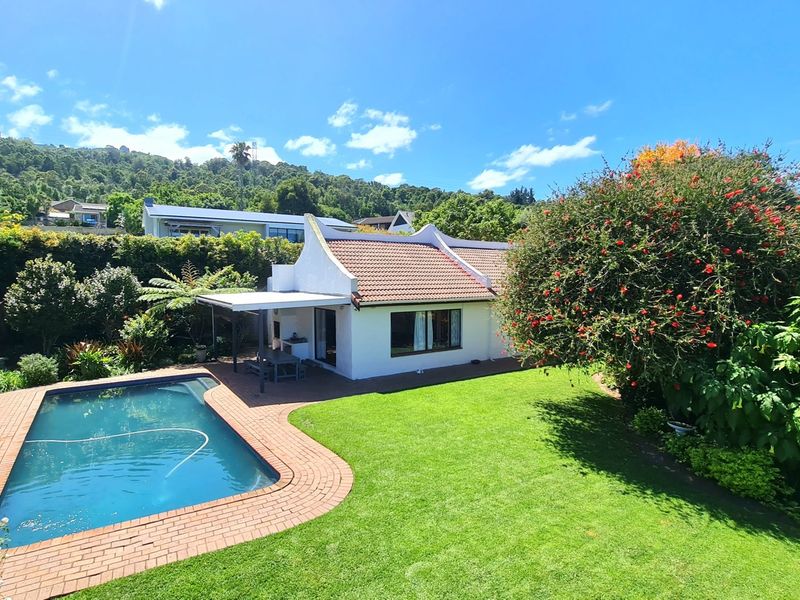 Rear view of the property featuring a swimming pool, brick-paved patio area, and a well-maintained garden with mature landscaping.