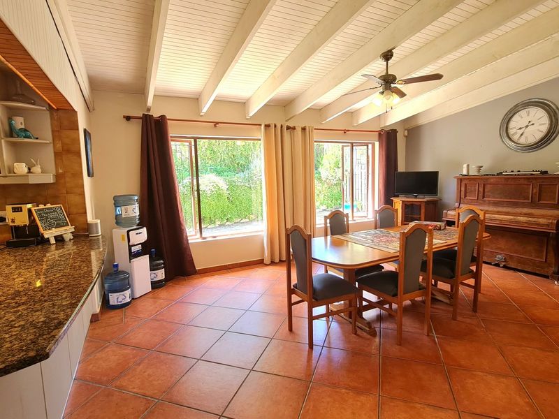 Spacious open-plan living and dining area featuring tiled floors, exposed beam ceilings, and a kitchen with granite countertops and built-in shelving.