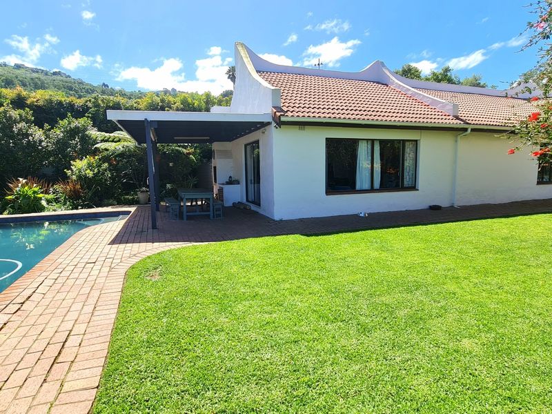 Rear view of the property featuring a well-maintained garden, swimming pool, and a covered patio area with a built-in braai.