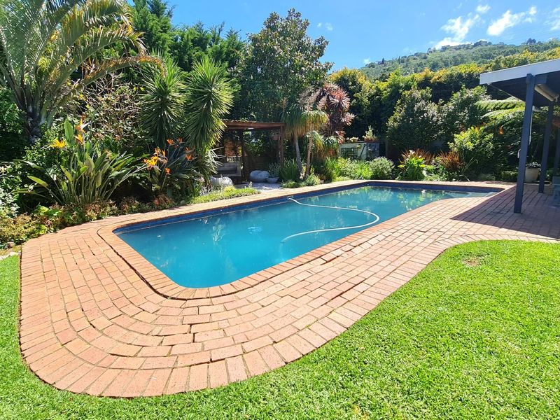A well-maintained outdoor pool area featuring brick coping, a lush landscaped garden, and an adjacent covered patio space.