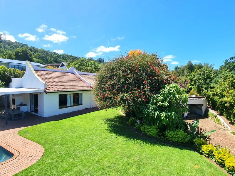 Rear view of the property featuring a swimming pool, covered patio with built-in braai, landscaped garden, and paved driveway.