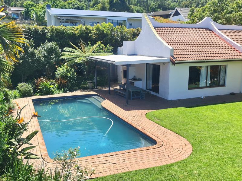 A well-maintained rear exterior view featuring a swimming pool with brick coping, a covered patio with a built-in braai, and a lush garden.