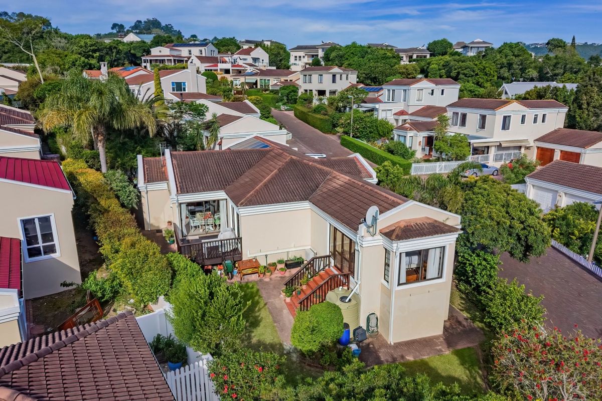 Aerial view of the property showcasing the tiled roof, rear patio area, wooden deck, and established garden within a residential estate setting.
