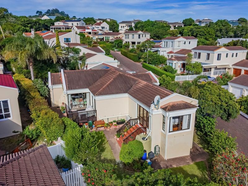 Aerial view of the property showcasing the tiled roof, rear patio area, wooden deck, and established garden within a residential estate setting.