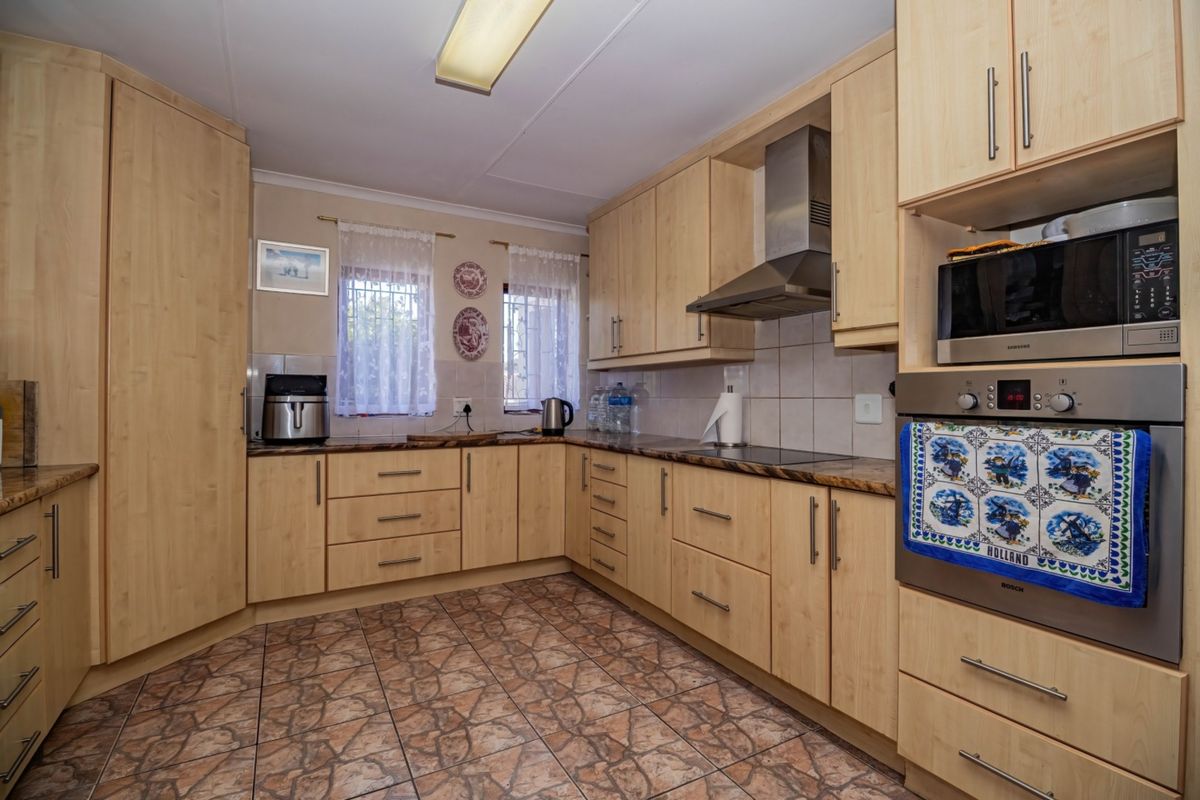 A functional kitchen featuring light wood-tone cabinetry, laminate countertops, tiled flooring, and integrated appliances including an oven, microwave, and extractor fan.