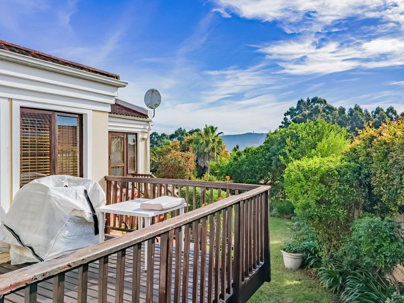 Elevated wooden deck balcony featuring a balustrade, sliding door access, and scenic garden views, offering a peaceful outdoor space for relaxation.