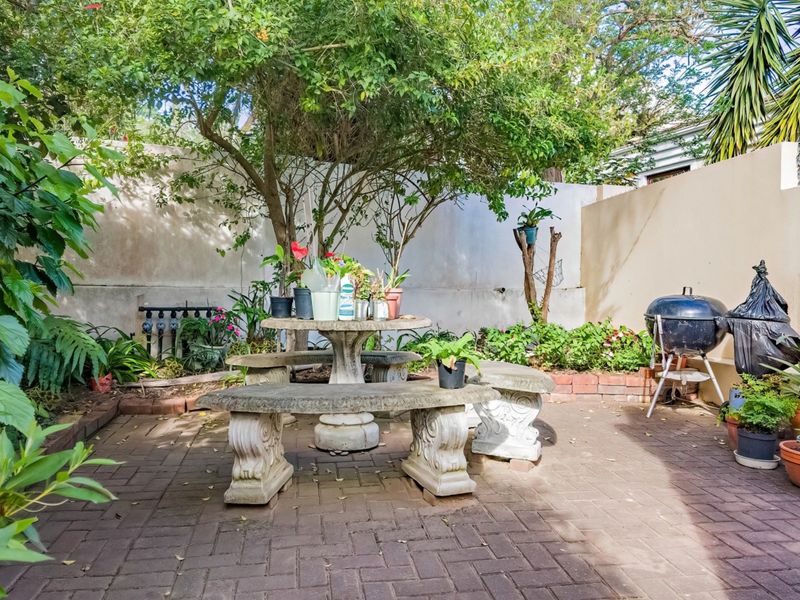 A private paved patio area featuring mature trees and boundary walls, offering a quiet outdoor space for relaxation and garden enjoyment.
