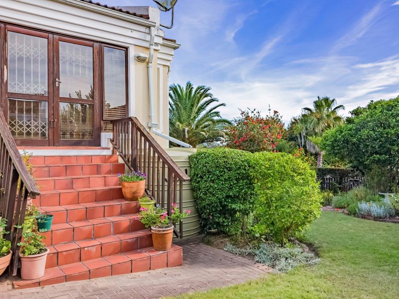 Rear exterior view featuring terracotta tiled stairs with timber handrails leading to glass doors, adjacent to a well-maintained garden and paved walkway.