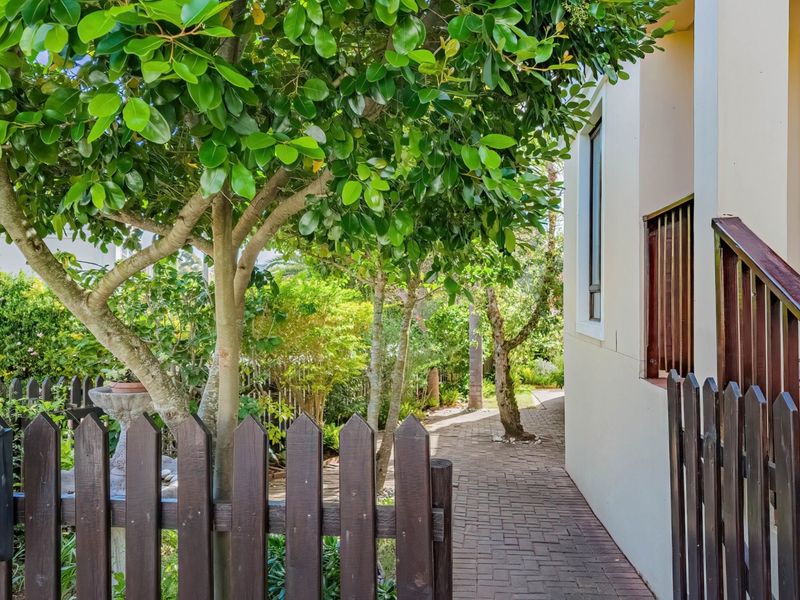 A well-maintained garden area featuring a paved walkway, mature trees, and a timber picket fence alongside the side elevation of the house.