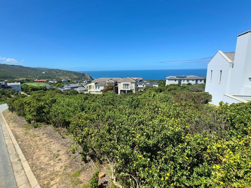 A scenic elevated view overlooking a residential estate with coastal landscape and ocean horizon in the background.