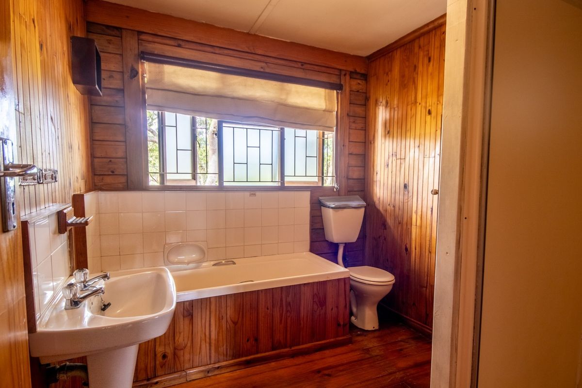 A dated bathroom featuring timber wall paneling, a pedestal basin, a built-in bathtub, and a toilet, with timber flooring throughout.