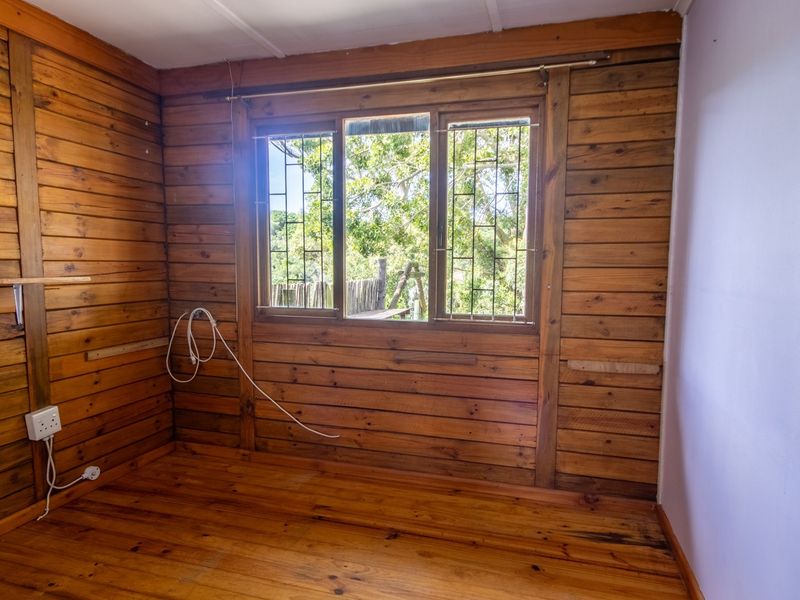 An empty bedroom featuring timber wall cladding and flooring, with security bars on the window and visible electrical fixtures.