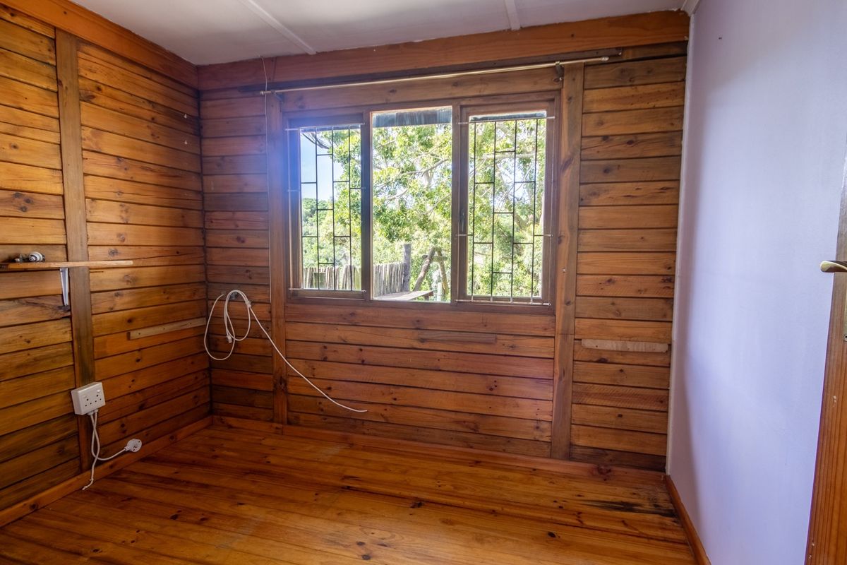 An empty bedroom featuring timber wall cladding and flooring, with security bars on the window and visible electrical fixtures.