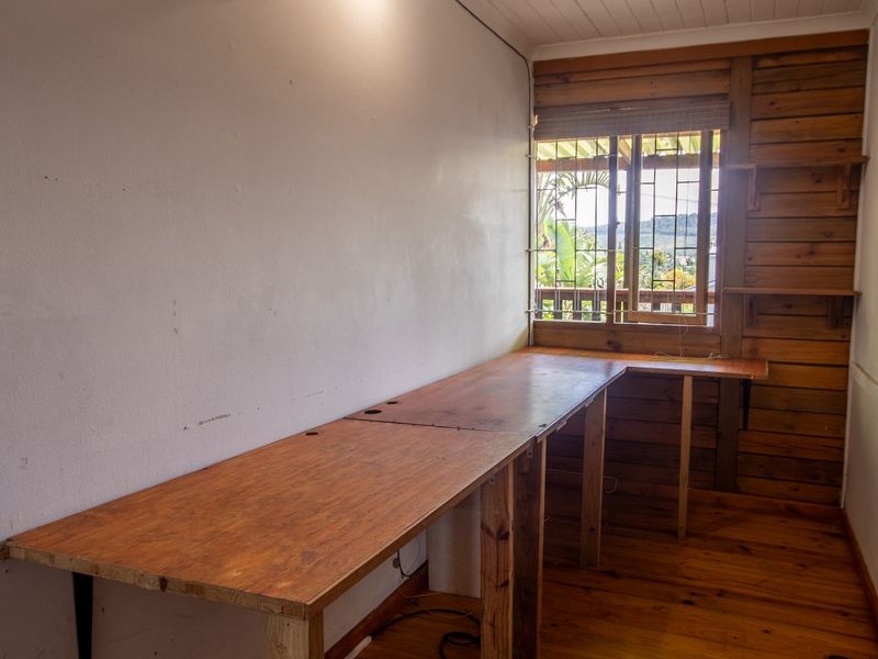 A functional home office space featuring built-in timber desk, wood-paneled wall accents, and natural timber flooring with security-fitted windows.