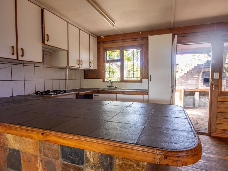 A dated kitchen featuring built-in cabinetry, a tiled breakfast bar, and a gas hob, with direct access to an outdoor patio area.