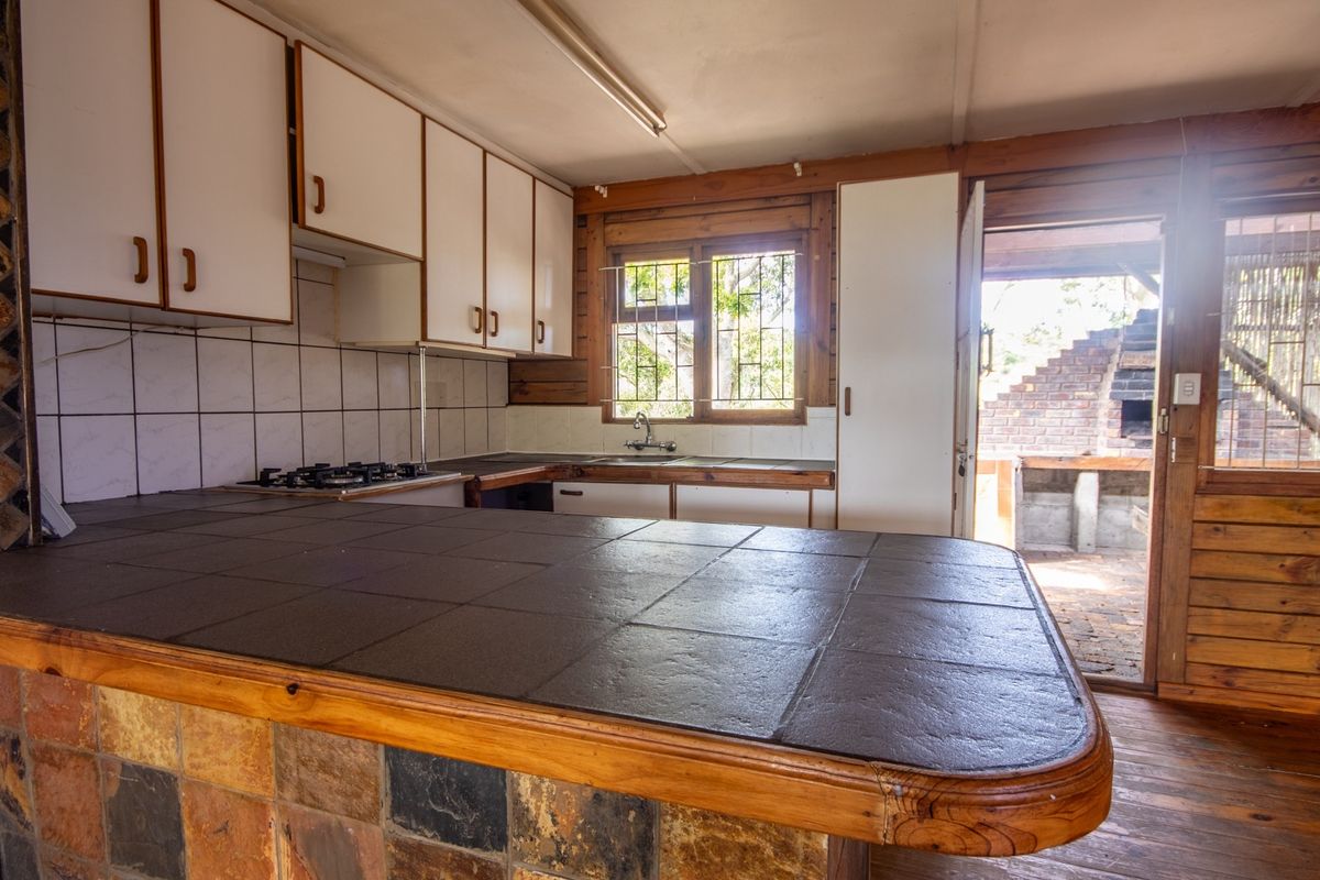 A dated kitchen featuring built-in cabinetry, a tiled breakfast bar, and a gas hob, with direct access to an outdoor patio area.