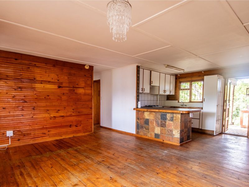 Open-plan living and kitchen area featuring timber wall cladding, wooden flooring, and a stone-tiled breakfast bar with built-in kitchen cabinetry.