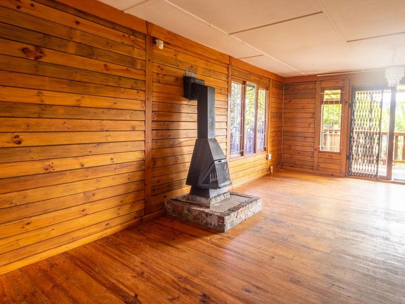 Spacious living area featuring warm wood paneling, polished hardwood floors, and a central freestanding fireplace with direct access to an outdoor deck.