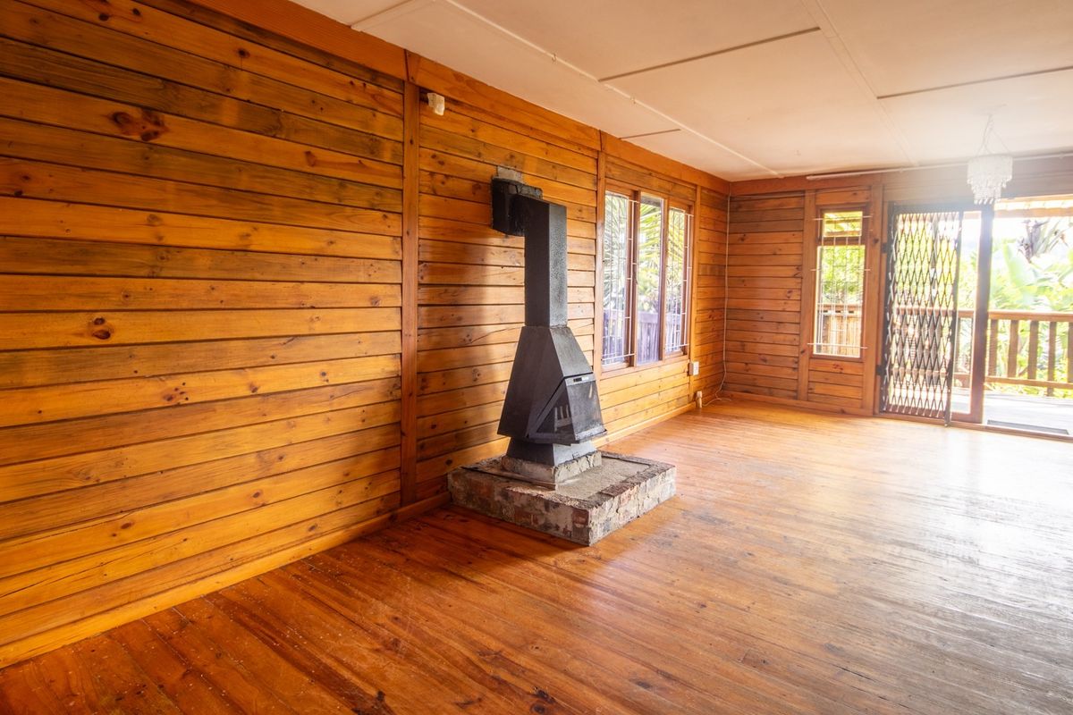 Spacious living area featuring warm wood paneling, polished hardwood floors, and a central freestanding fireplace with direct access to an outdoor deck.