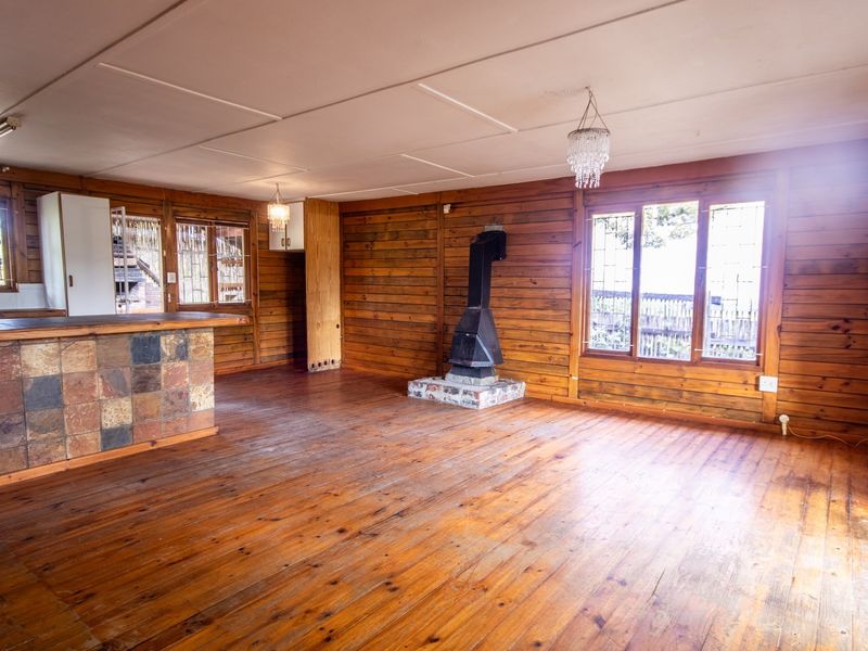 Spacious open-plan living area featuring timber wall paneling, hardwood floors, a central freestanding fireplace, and a tiled breakfast bar with access to outdoor space.