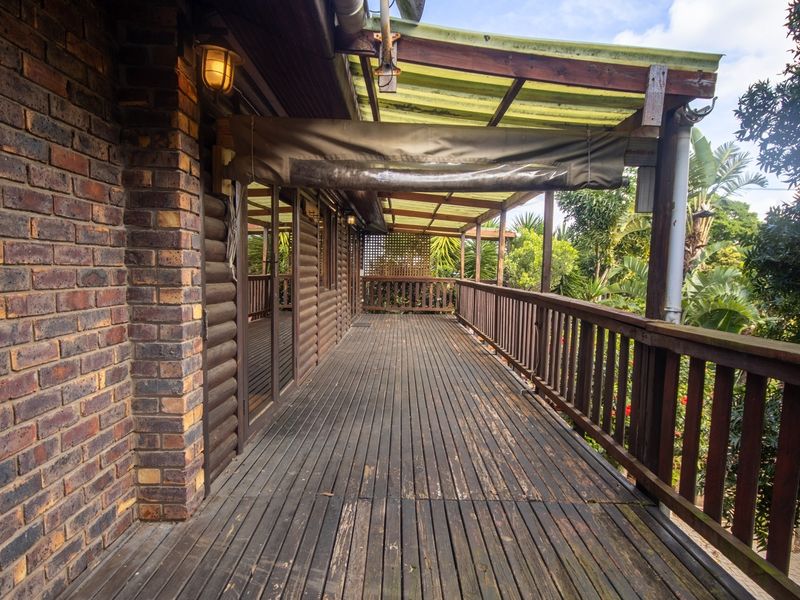A spacious covered timber deck featuring a balustrade and brick wall, offering a functional outdoor space in need of maintenance and refinishing.