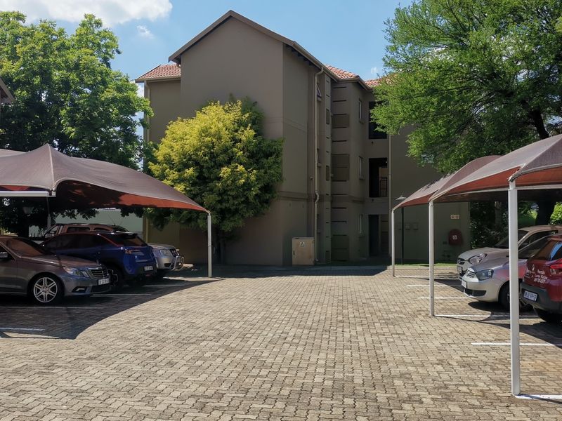 Exterior view of the townhouse complex featuring a paved parking area with shade cloth carports and multi-story residential units.