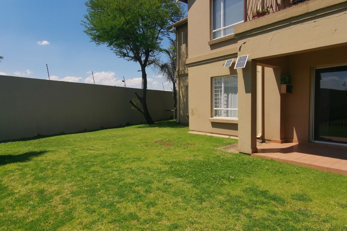 Rear view of the townhouse featuring a private garden, tiled patio area, and secure perimeter wall with electric fencing.