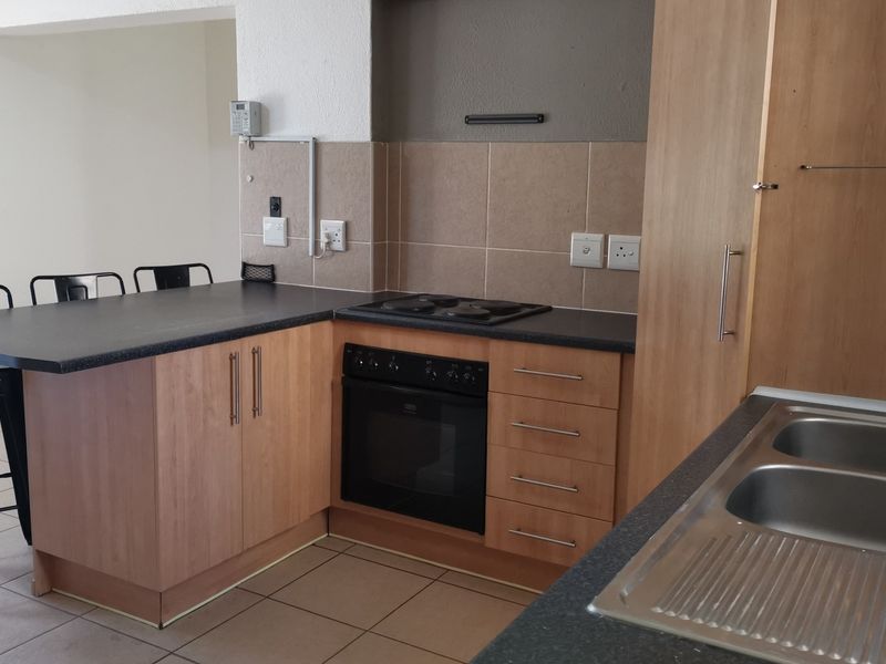 Functional kitchen featuring laminate cabinetry, built-in oven, electric hob, double bowl stainless steel sink, and a convenient breakfast bar area.
