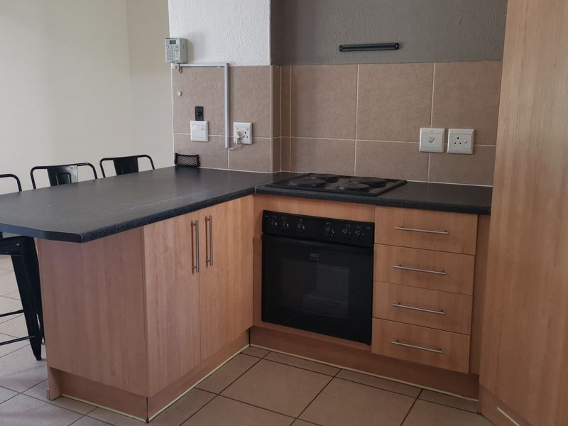 Compact kitchen featuring light wood cabinetry, dark laminate countertops, built-in oven and hob, and tiled backsplash with breakfast bar seating area.