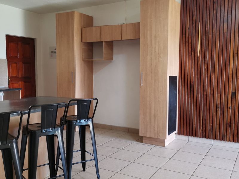 Open plan living area featuring a kitchen island, built-in cabinetry, and a decorative timber slat wall feature with tiled flooring throughout.