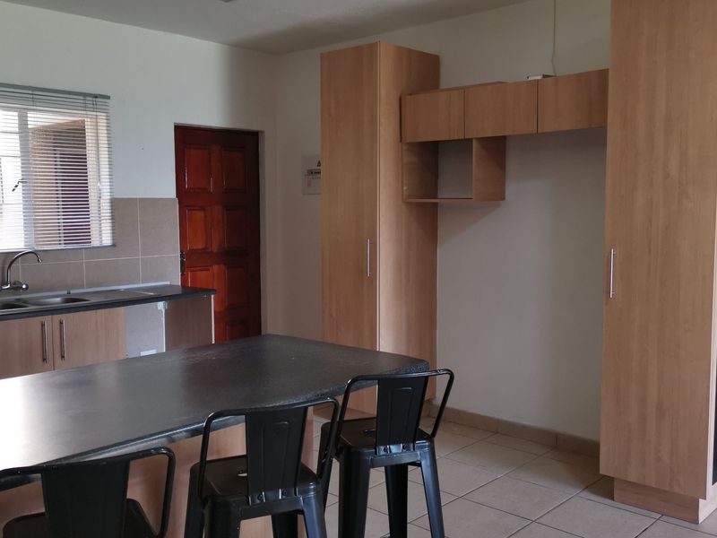 A functional kitchen featuring light wood cabinetry, dark laminate countertops, a tiled backsplash, and tiled flooring with a breakfast bar area.