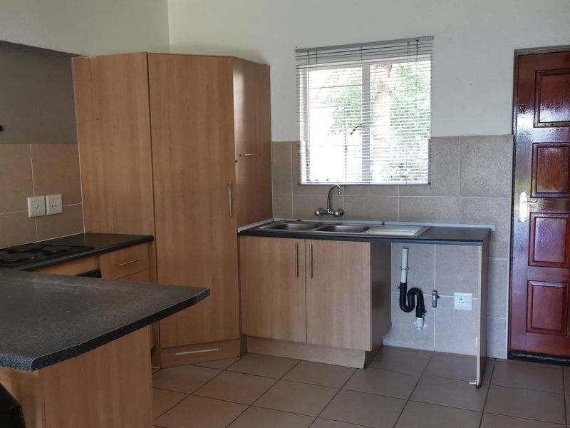 A functional kitchen featuring laminate cabinetry, tiled splashbacks, a built-in hob, and a double bowl sink with an open plumbing area.