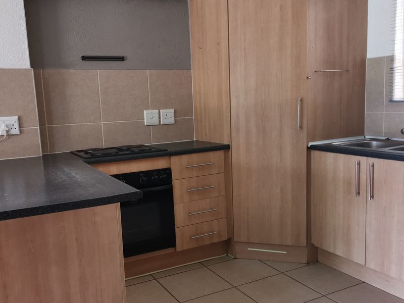 A functional kitchen featuring light wood-finish cabinetry, dark countertops, a built-in oven and hob, and a double basin sink with tiled backsplash.